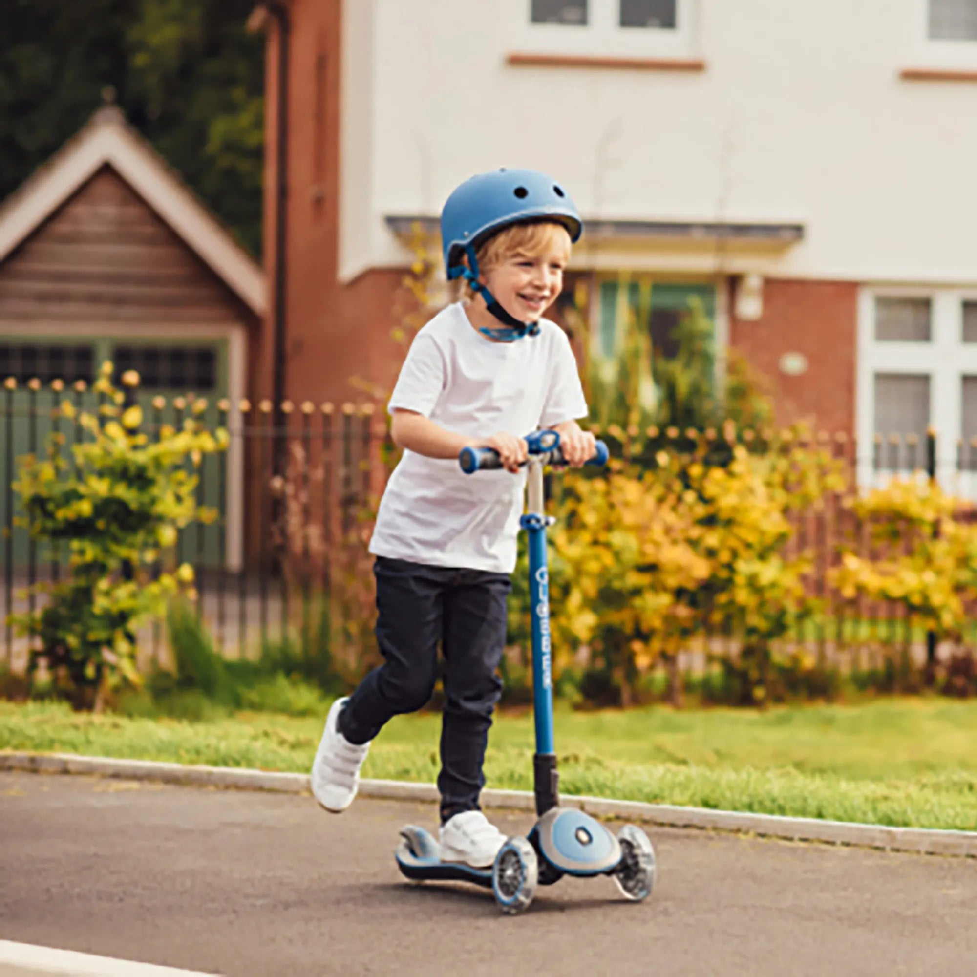 Smiling boy riding a lime green elite deluxe foldable and adjustable 3 wheel scooter wearing globbers primo navy blue helmet.