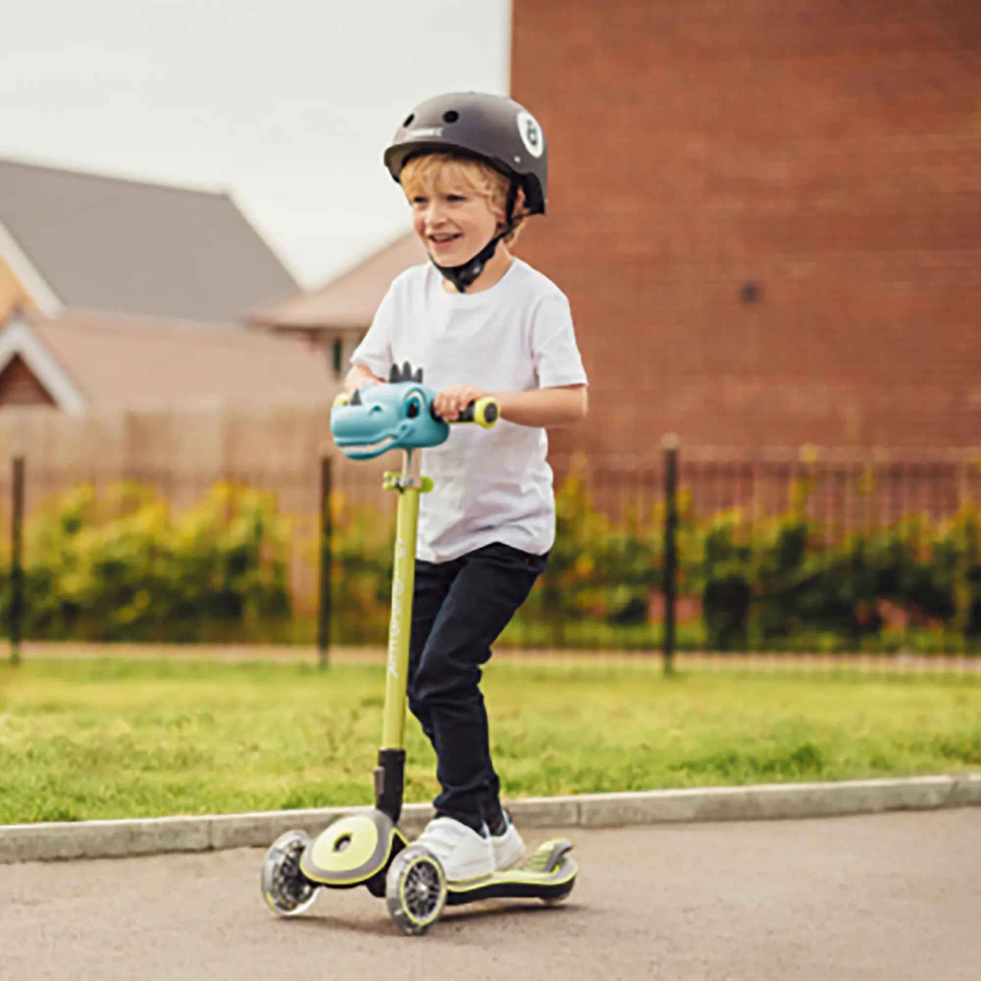 Smiling boy riding a lime green elite deluxe scooter with Dinosaur head t bar accessory wearing a globber primo black helmet.